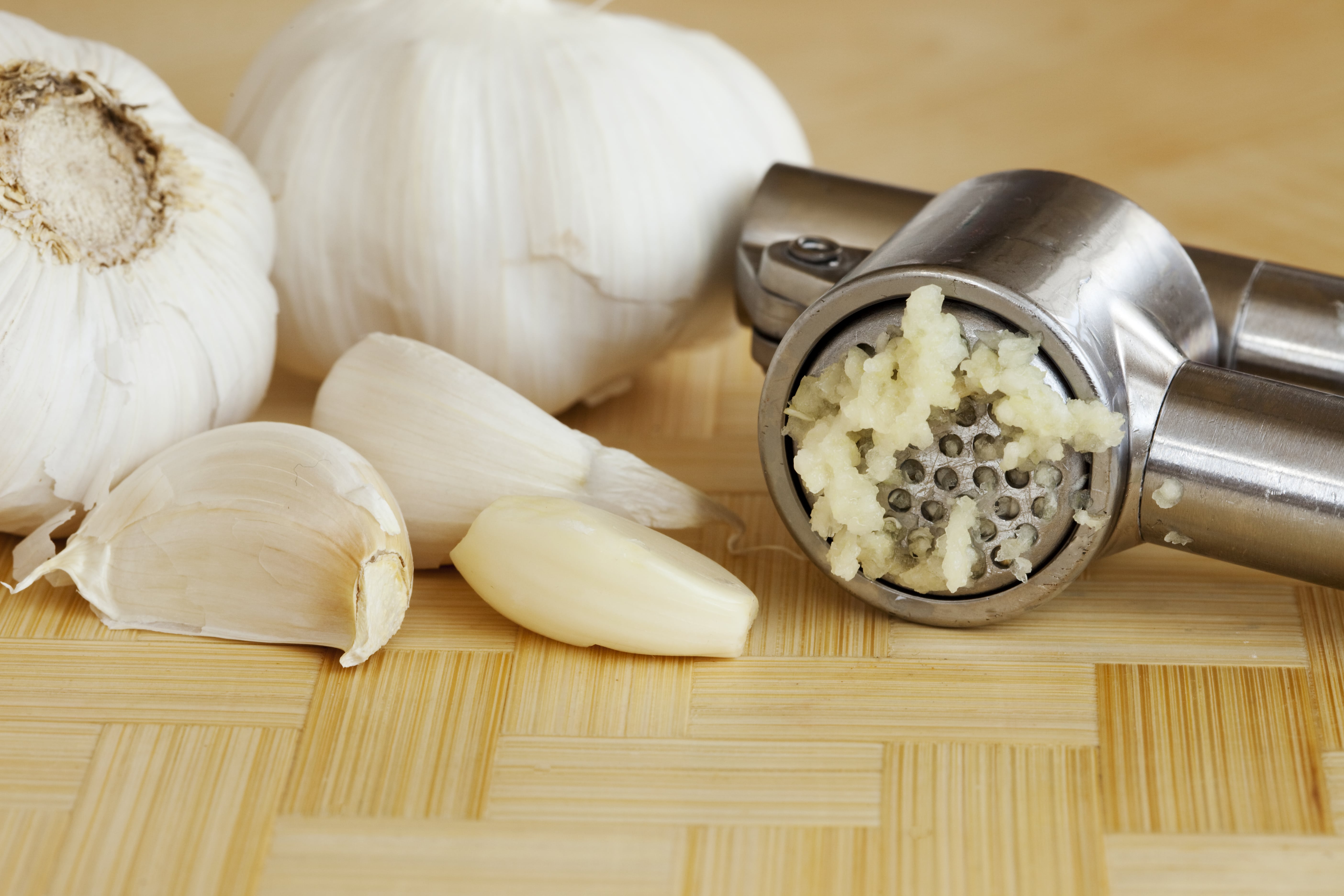 Garlic cloves and a garlic press on a wooden cutting board